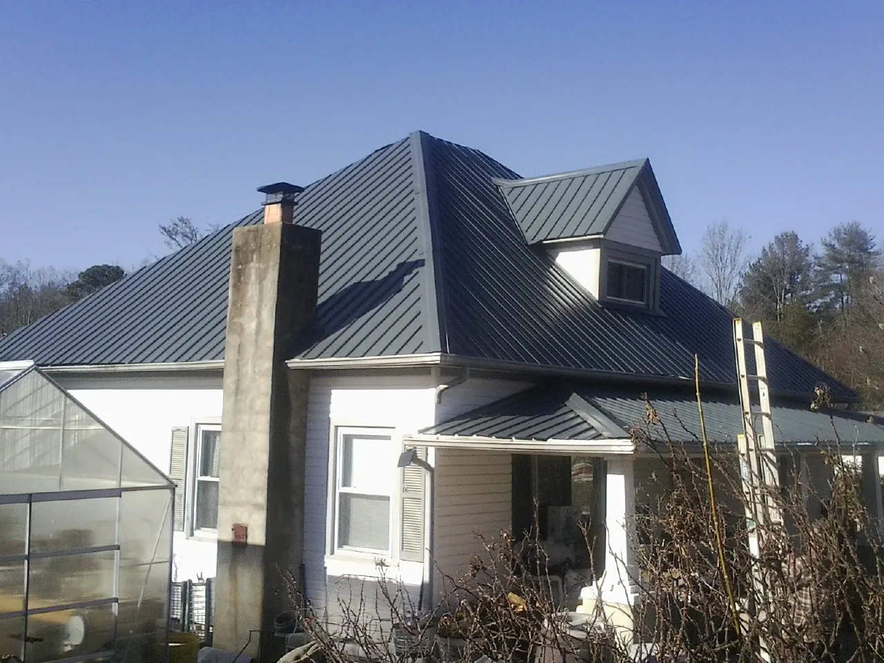 Dark blue standing seam metal roof on a white farmhouse with dormer — Slate & Tile Roof Repair by Roofing Brothers in Belpre