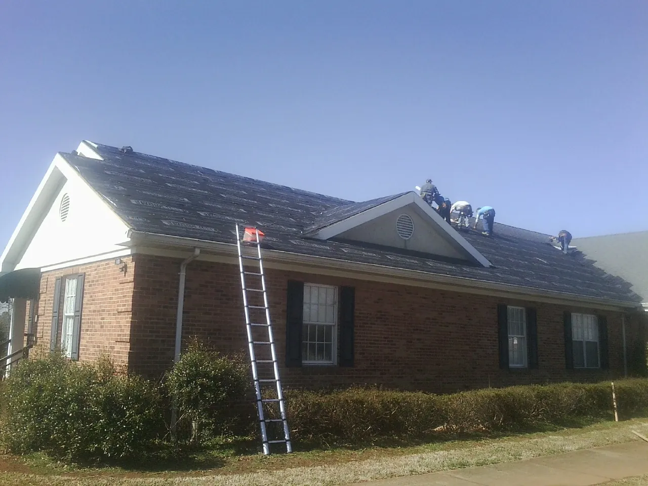 Crew tearing shingles off a brick ranch roof with a ladder set — Emergency Roof Repair work by our crew in Belpre