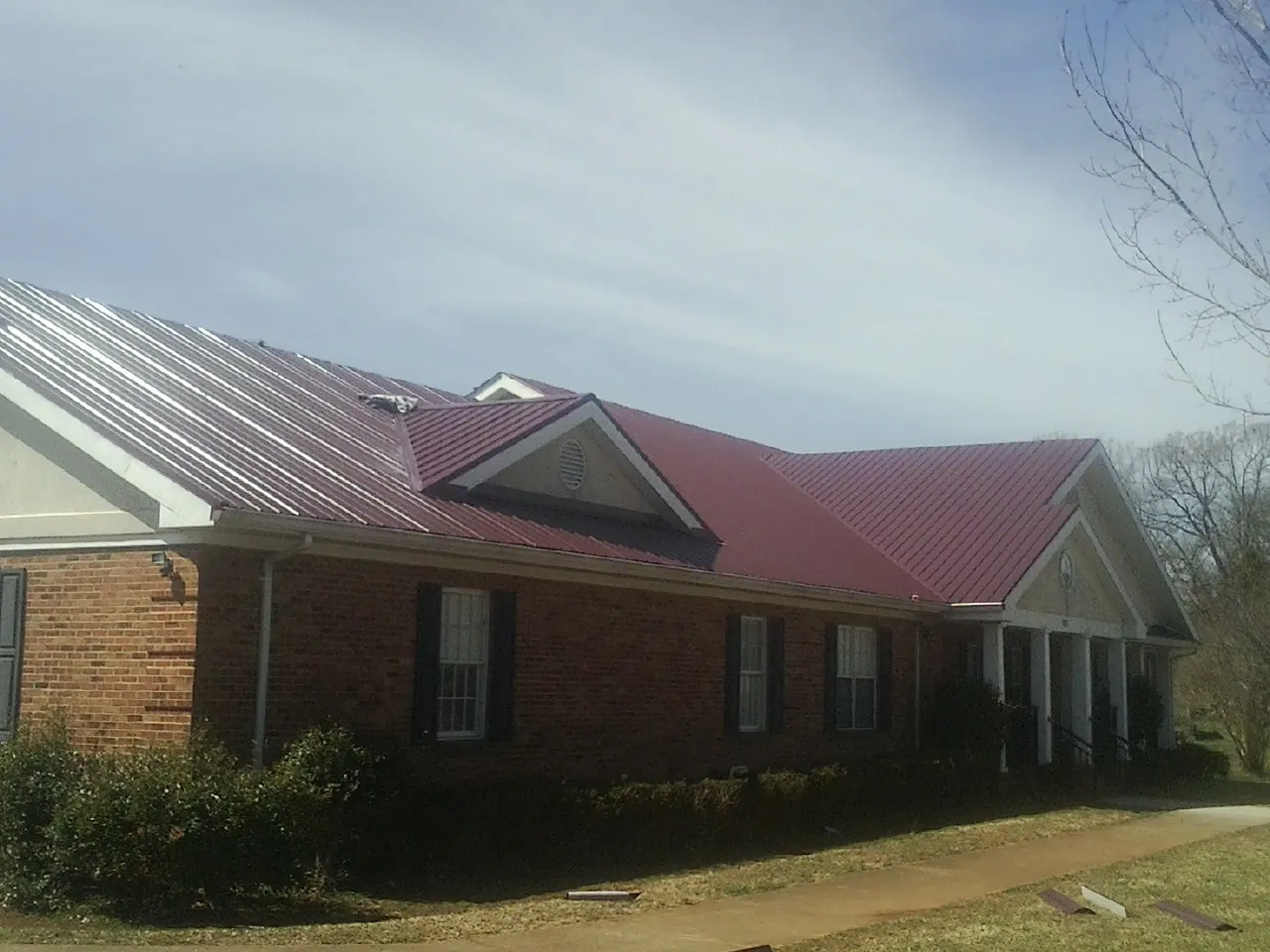 Red metal roof with gabled entries on a long brick building, from a Hail Damage Roof Repair job in Belpre