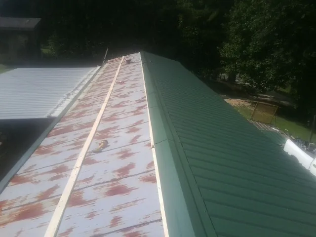 Old rusted panels beside newly installed green metal roofing — Wind Damage Roof Repair by Roofing Brothers in Belpre