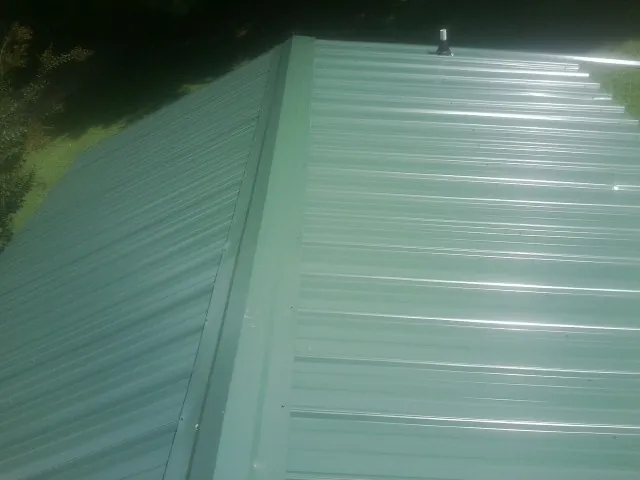 New green metal panels meeting at the ridge of a roof — Flat Roof Repair work by our crew in Belpre