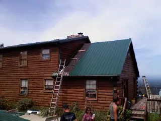 Green metal roof going on a two story log home with ladders set in Belpre