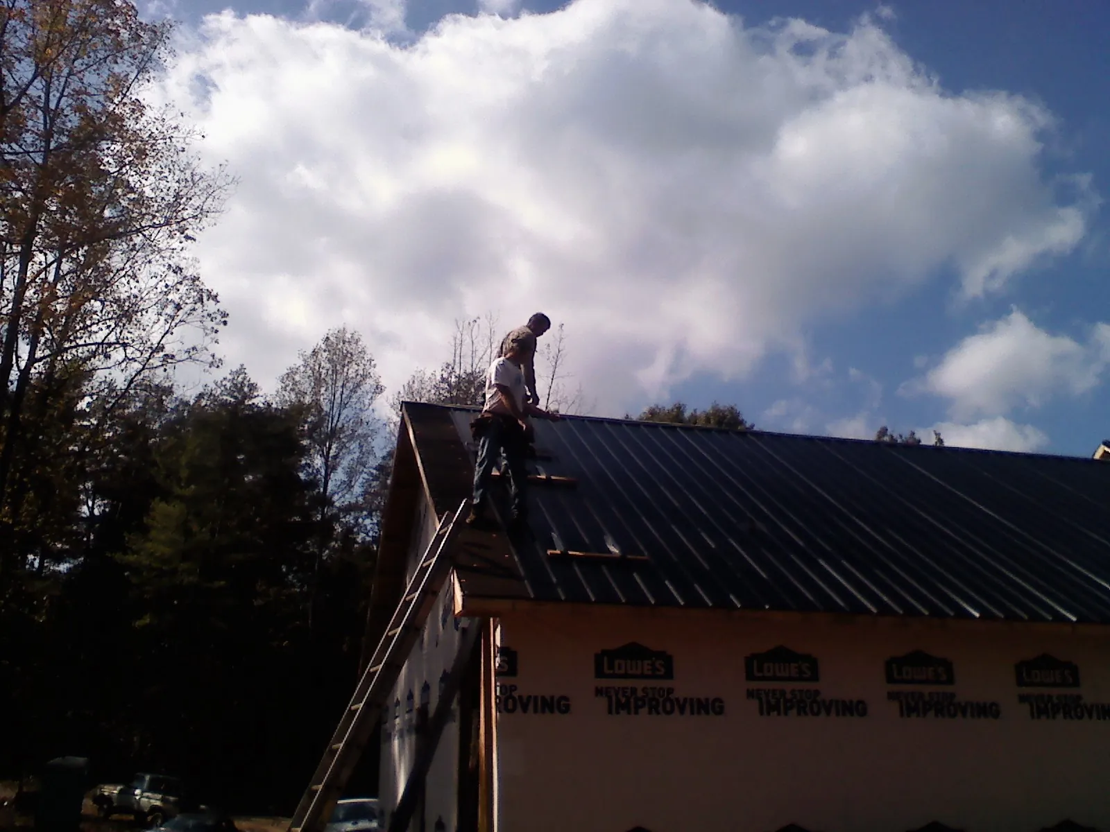 Roofer fastening dark metal panels high against a cloudy sky, from a Roof Inspection job in Belpre