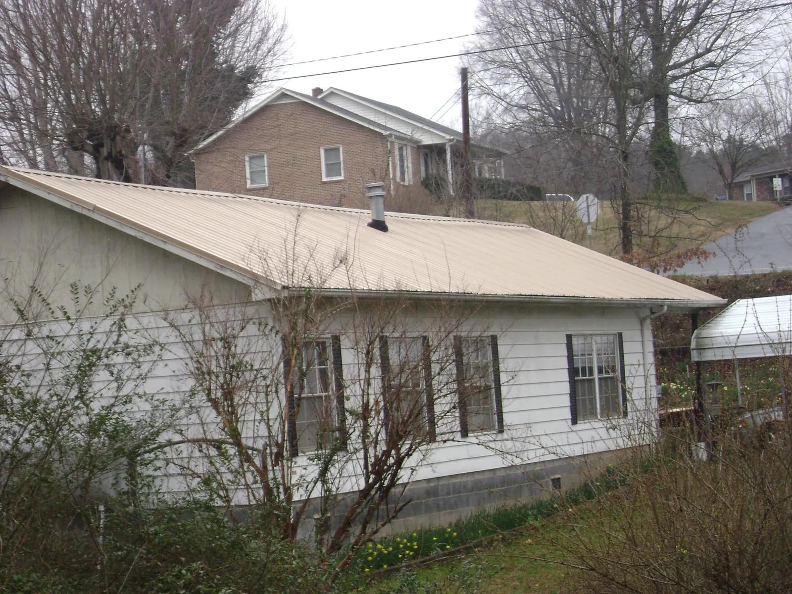 Tan metal roof on a white sided house set into a hillside — Commercial Roofing by Roofing Brothers in Belpre