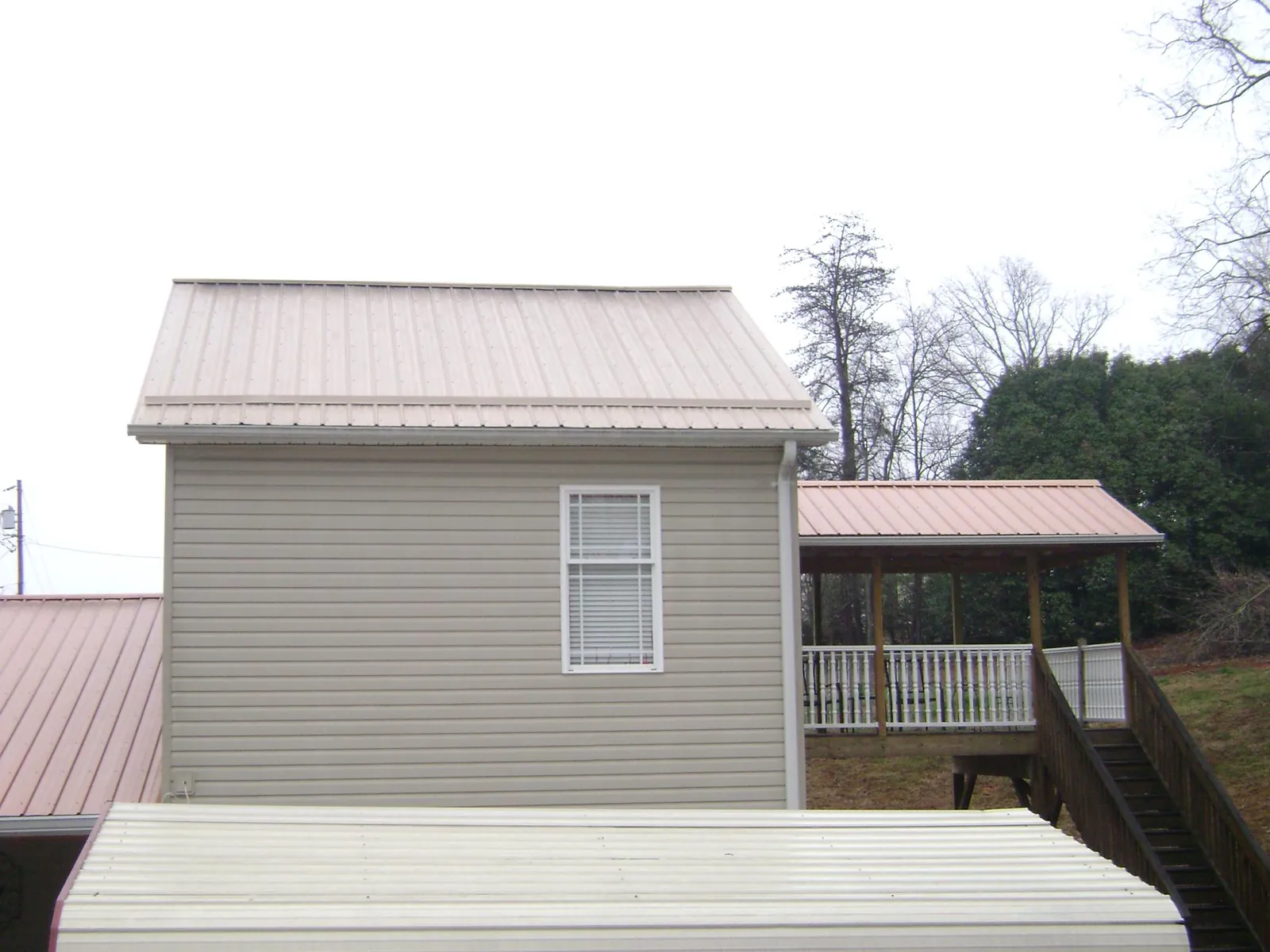 Tan metal roofs on a two story addition and attached porch, from a Roof Replacement job in Belpre